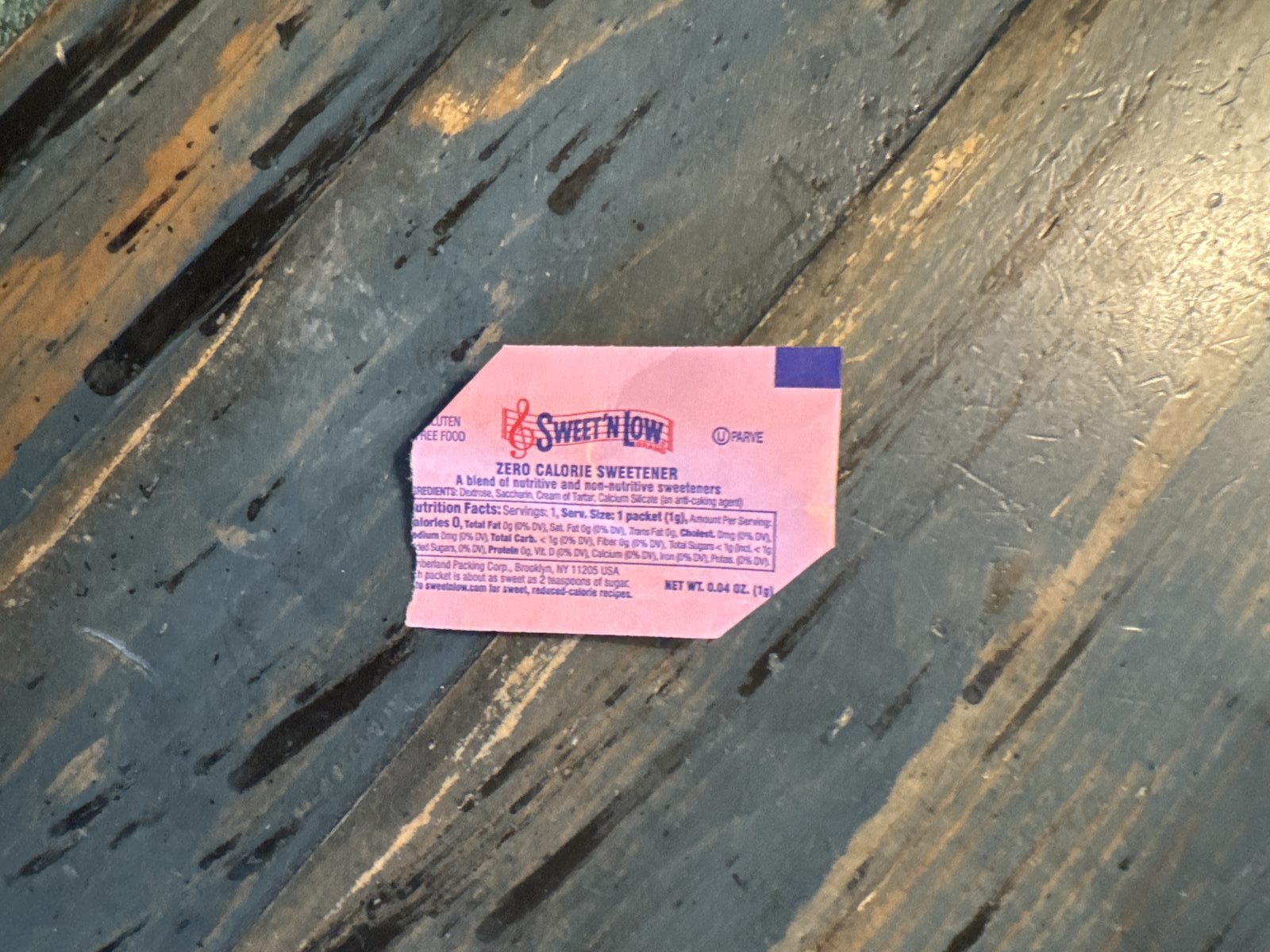 A Sweet'N Low packet with two corners torn off, lying on a scarred blue workbench